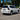 This daytime scene shows a white 2018 Lexus GX460 from the rear three-quarter angle. The vehicle is fitted with unlit PRISMBEAM LED tail lights featuring dark red panels, smoked internal light bars, and clear lower sections.