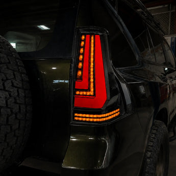 Illuminated PRISMBEAM LED tail light shown in a darkened automotive workshop close-up.