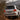 White Toyota Land Cruiser with illuminated LED tail lights climbing a steep dirt trail behind foreground branches.