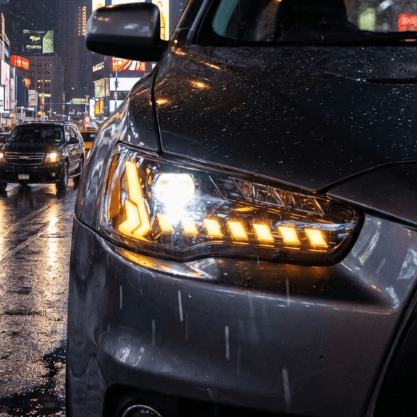 Car headlight on a rainy city street with wet road and illuminated signs in the background