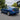 This daytime scene shows a blue 2006–2011 Honda Civic sedan fitted with PRISMBEAM RGB tail lights. The rear three-quarter view displays the multicolor light signatures, smoked housings, rear spoiler, and surrounding landscaped parking environment.