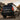 A modified black Lexus GX460 is shown from a low rear three-quarter angle in an outdoor setting. The SUV features illuminated red and amber PRISMBEAM LED tail lights, off-road tires, black wheels, raised suspension, and roof-mounted equipment.