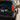 A close rear three-quarter view shows half of a black Lexus GX 470 parked in a residential driveway. The installed tail light features a red illuminated field, amber L-shaped LED strip, segmented red column, and lower amber and white sections.