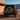 A dark Toyota Land Cruiser Prado rear-door conversion is shown outside a modern desert residence. The SUV features a rear-mounted spare tire and illuminated PRISMBEAM tail lights with red panels and amber LED elements.