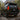 A dark Toyota Land Cruiser Prado is shown from the rear three-quarter angle at an evergreen mountain campsite. Its illuminated PRISMBEAM tail lights feature red panels, vertical amber LED elements, and dual lower amber light bars.