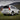 A white Lexus GX 470 is shown from a rear three-quarter angle in a mountain meadow. Its upgraded tail lights display red illuminated panels, amber L-shaped guides, and amber lower light strips.
